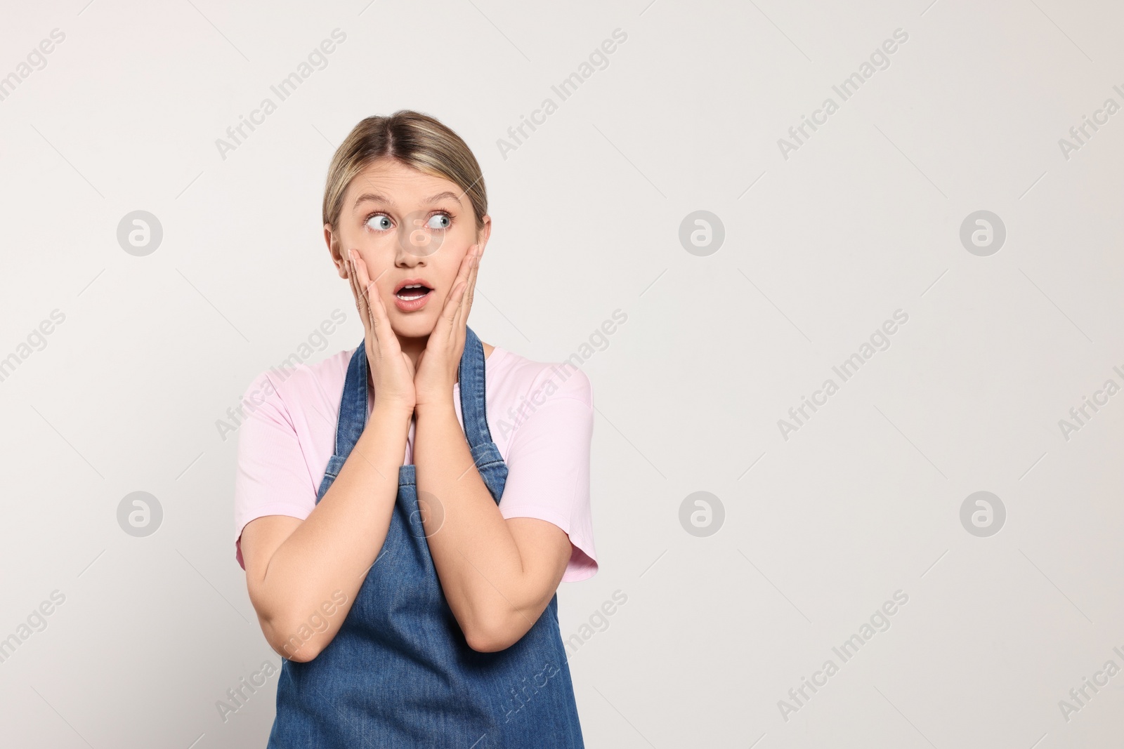 Photo of Beautiful young woman in denim apron on light grey background. Space for text