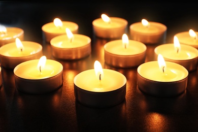 Wax candles burning on table in darkness, closeup