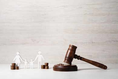 Photo of Divorce concept. Gavel, wedding rings, coins and paper cutout of family on white wooden table, space for text