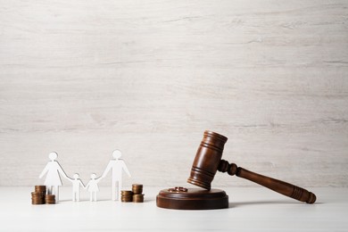 Divorce concept. Gavel, wedding rings, coins and paper cutout of family on white wooden table, space for text