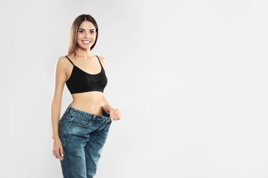 Photo of Attractive young woman with slim body wearing her old big jeans on white background. Space for text