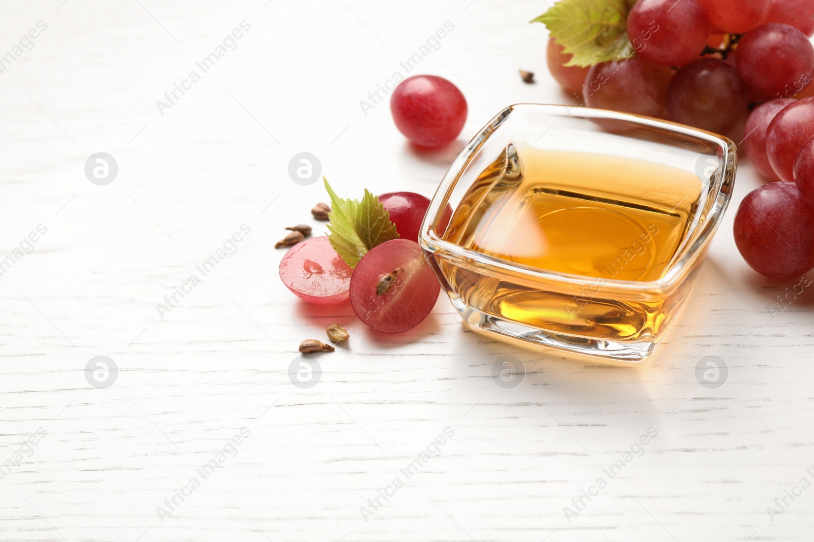 Photo of Glass bowl with natural grape seed oil on white wooden table, space for text. Organic cosmetic