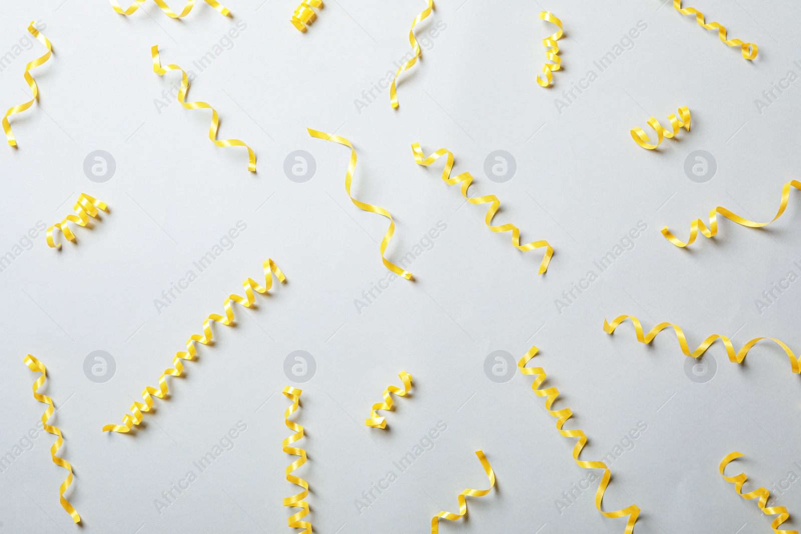 Photo of Yellow serpentine streamers on light background, flat lay