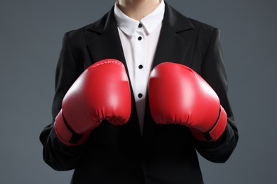 Photo of Businesswoman in suit wearing boxing gloves on grey background, closeup