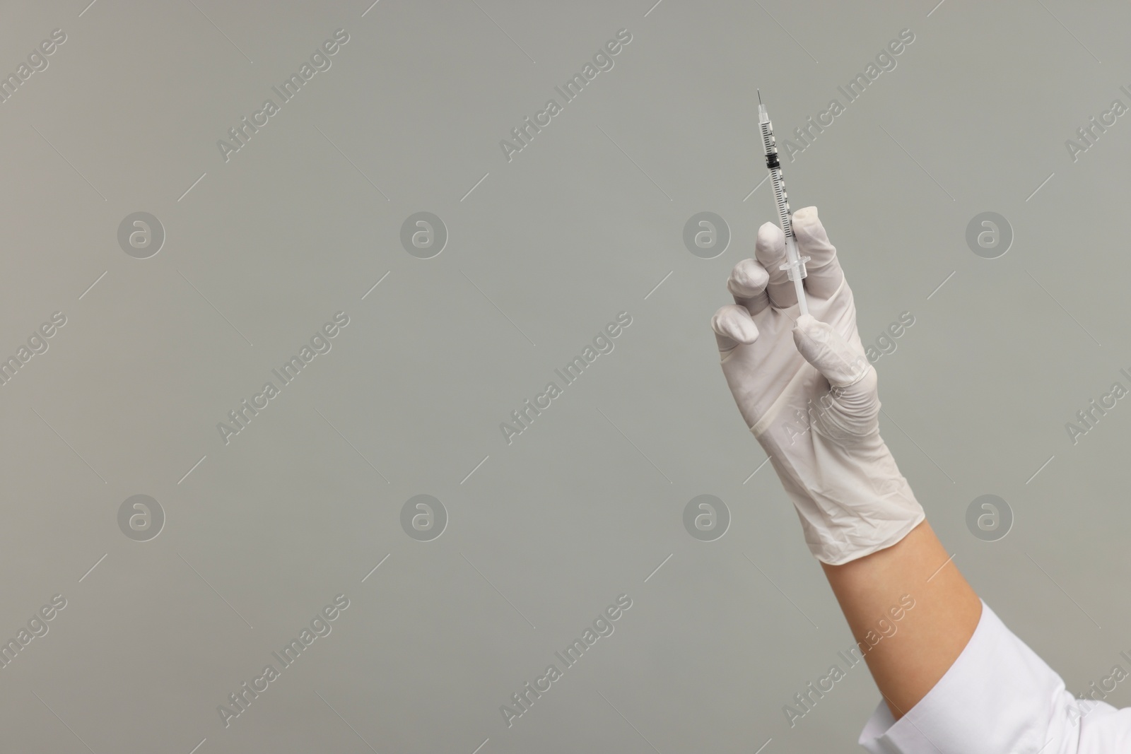 Photo of Doctor holding medical syringe on grey background, closeup. Space for text