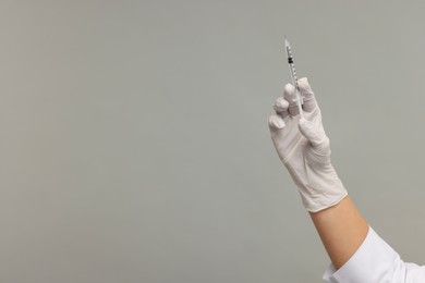 Doctor holding medical syringe on grey background, closeup. Space for text