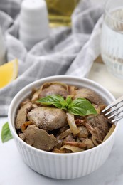 Photo of Delicious fried chicken liver with onion and basil in bowl on white table