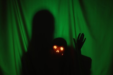 Silhouette of creepy ghost with skull behind dark green cloth
