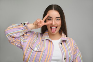 Photo of Happy woman showing her tongue and V-sign on gray background