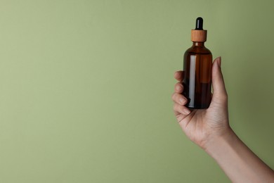 Woman holding bottle of cosmetic product on pale olive background, closeup. Space for text