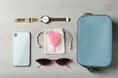 Flat lay composition with menstrual cup and different women's accessories on white wooden table