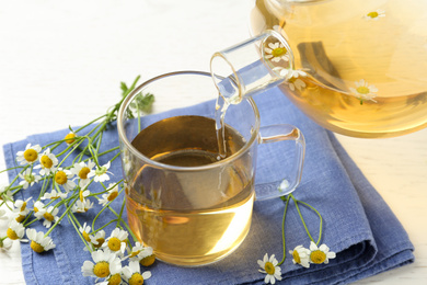 Photo of Pouring tasty chamomile tea into cup on table