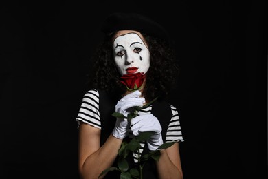 Young woman in mime costume with red rose posing on black background