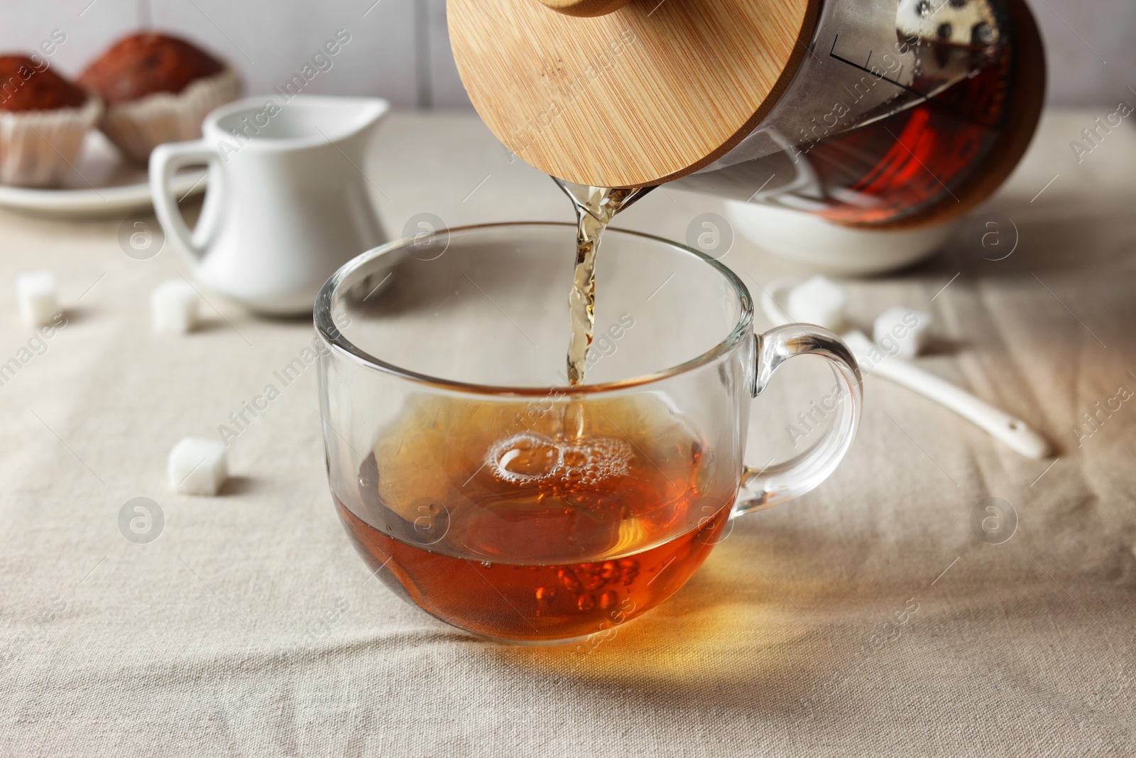 Photo of Pouring warm tea into cup on light table, closeup