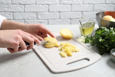 Photo of Woman cutting boiled potatoes at white table, closeup. Cooking vinaigrette salad