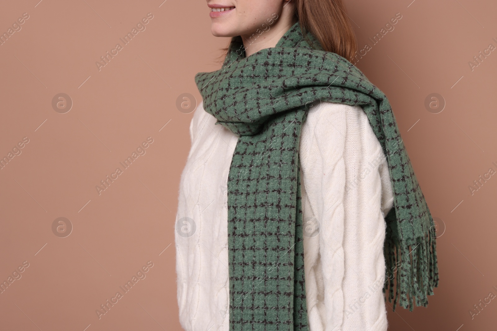 Photo of Beautiful woman in warm scarf on brown background, closeup. Space for text