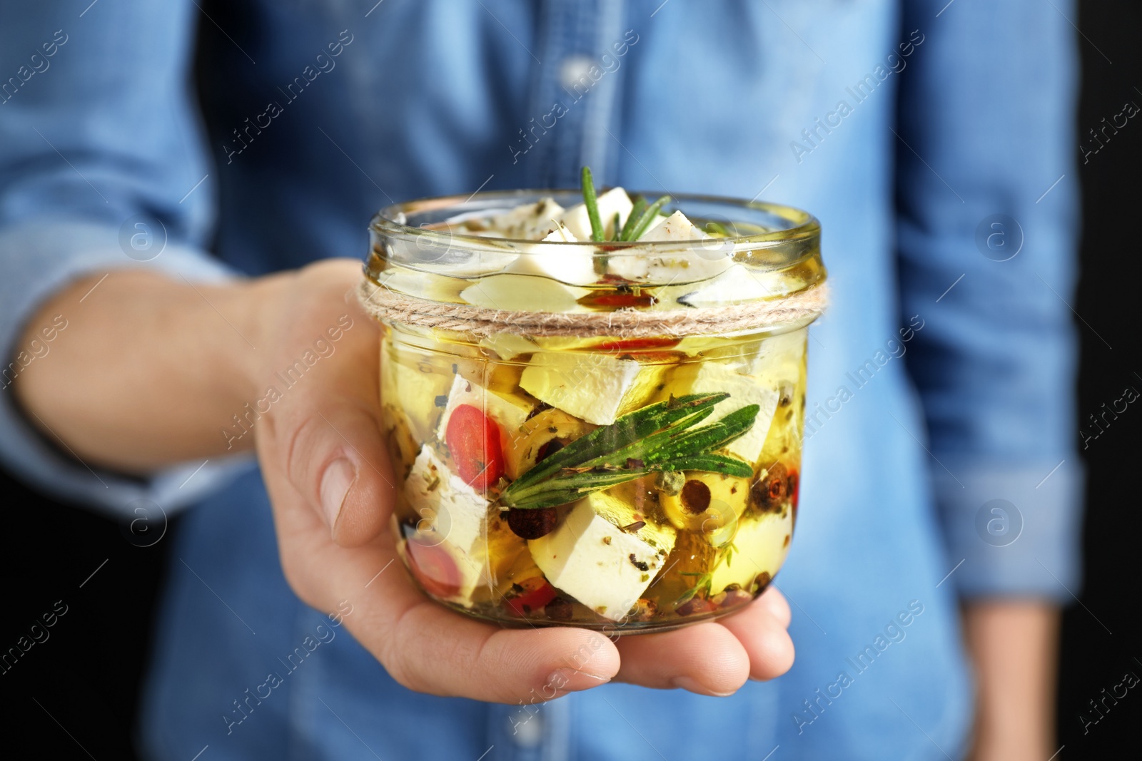 Photo of Woman holding jar with pickled feta cheese on black background, closeup