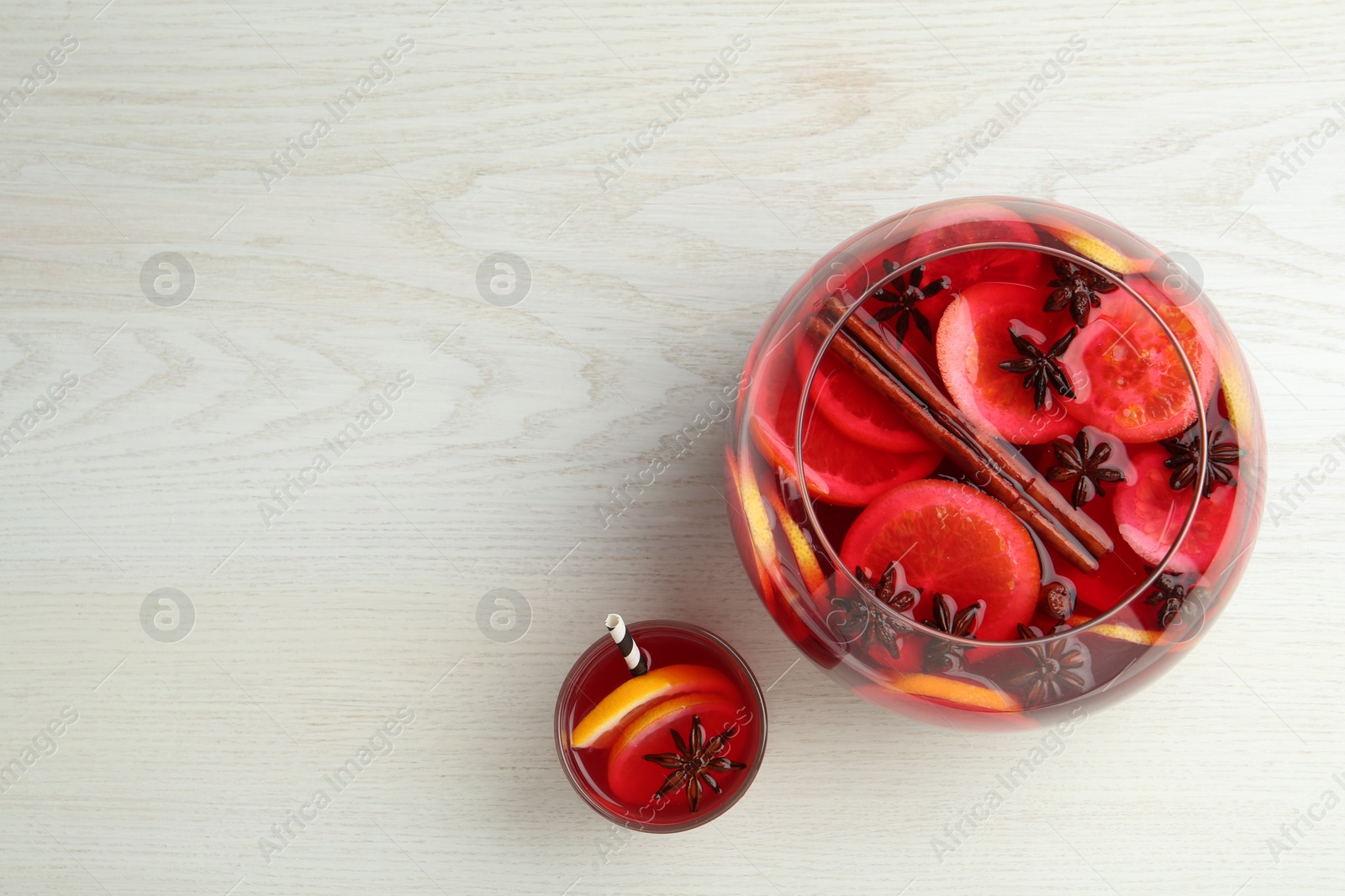 Photo of Glass and bowl of delicious aromatic punch drink on white wooden table, flat lay. Space for text