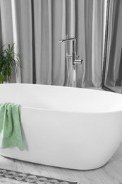 Photo of Stylish white tub with towel in bathroom. Interior design