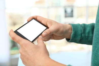 Photo of Man holding smartphone with blank screen on blurred background, closeup of hands. Space for text