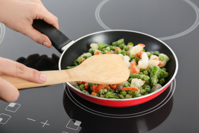 Photo of Woman cooking frozen vegetable mix on induction stove, closeup