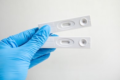 Photo of Doctor in gloves holding disposable express tests for hepatitis on white background, closeup