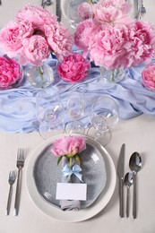 Photo of Stylish table setting with beautiful peonies, napkin and blank card, above view