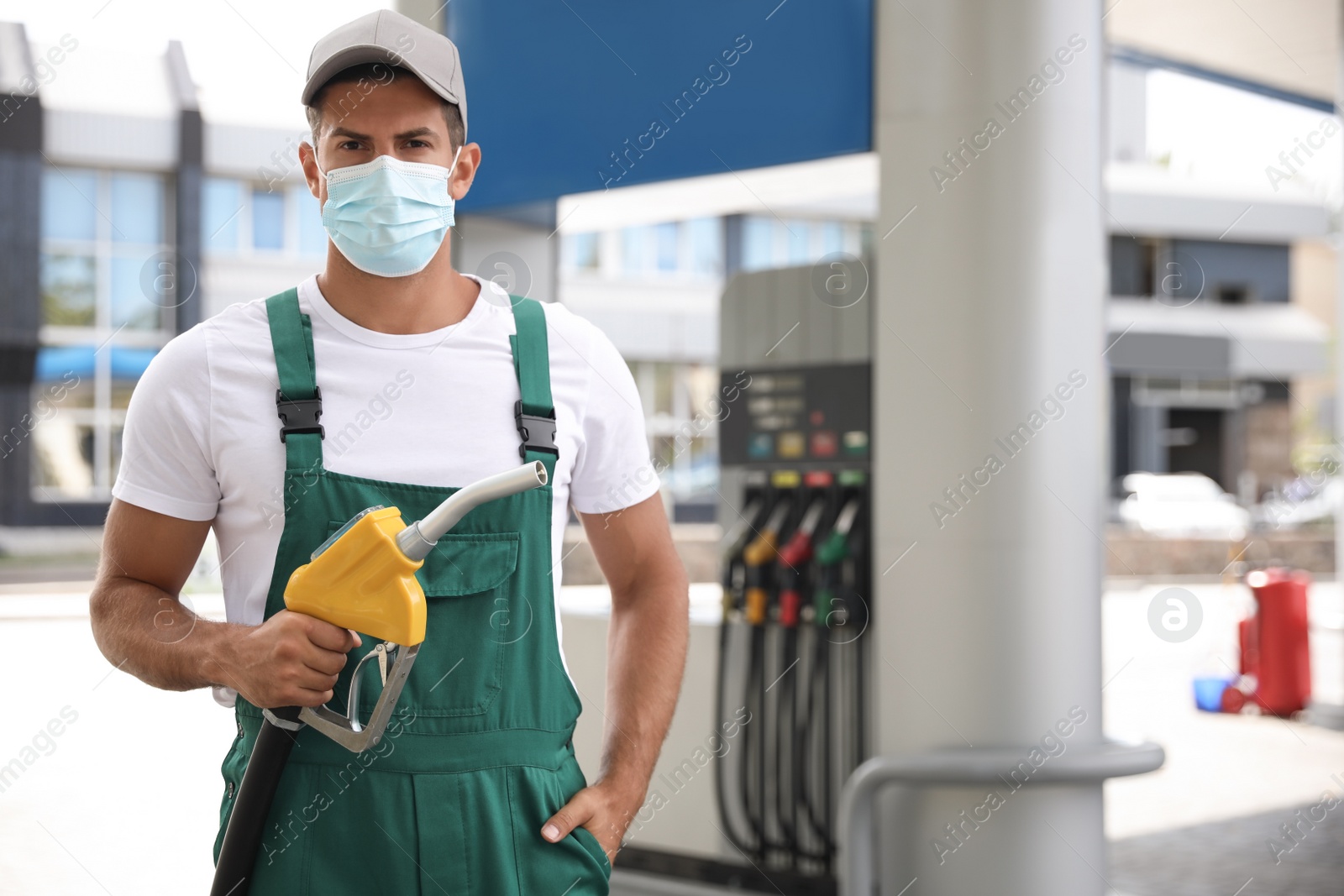 Photo of Worker in mask with fuel pump nozzle at modern gas station