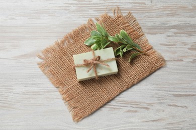 Soap bar and green plant on wooden table, top view