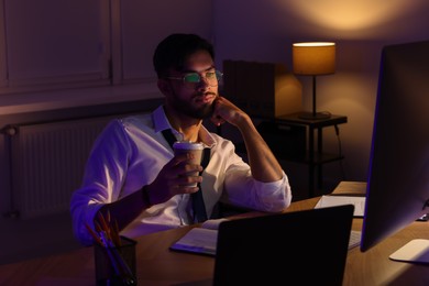 Photo of Tired man with coffee working late in office