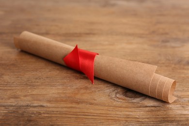 Rolled student's diploma with red ribbon on wooden table