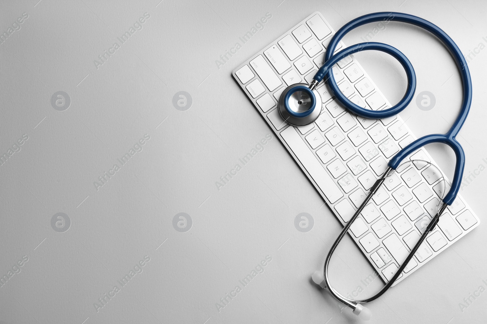 Photo of Keyboard and stethoscope on light grey background, flat lay with space for text. Concept of technical support