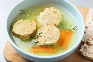 Photo of Board with bowl of Jewish matzoh balls soup on table, closeup