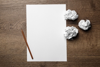 Blank sheet and crumpled paper balls on wooden table, flat lay. Space for text