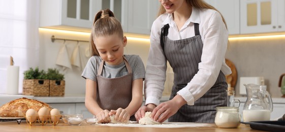 Photo of Making bread. Mother and her daughter kneading dough at wooden table in kitchen