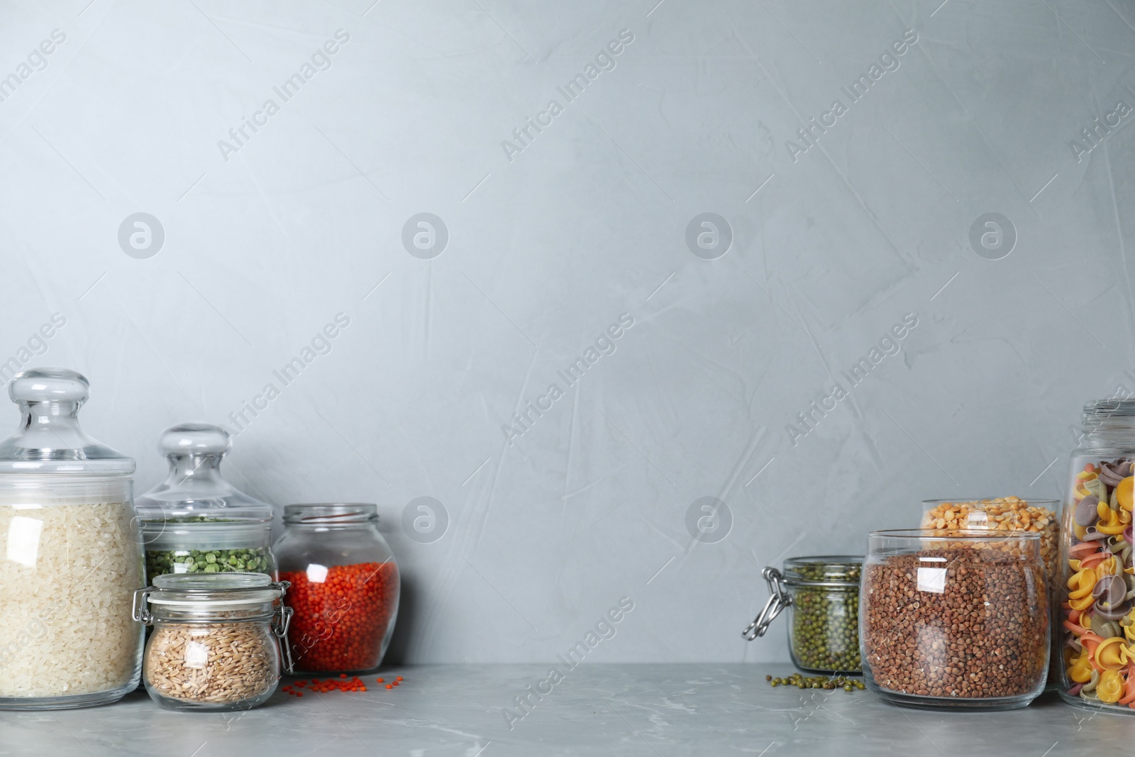 Photo of Glass jars with different types of groats on grey marble table