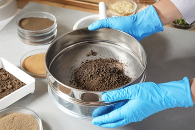 Photo of Scientist pulverizing and sieving soil samples at table, closeup. Laboratory analysis