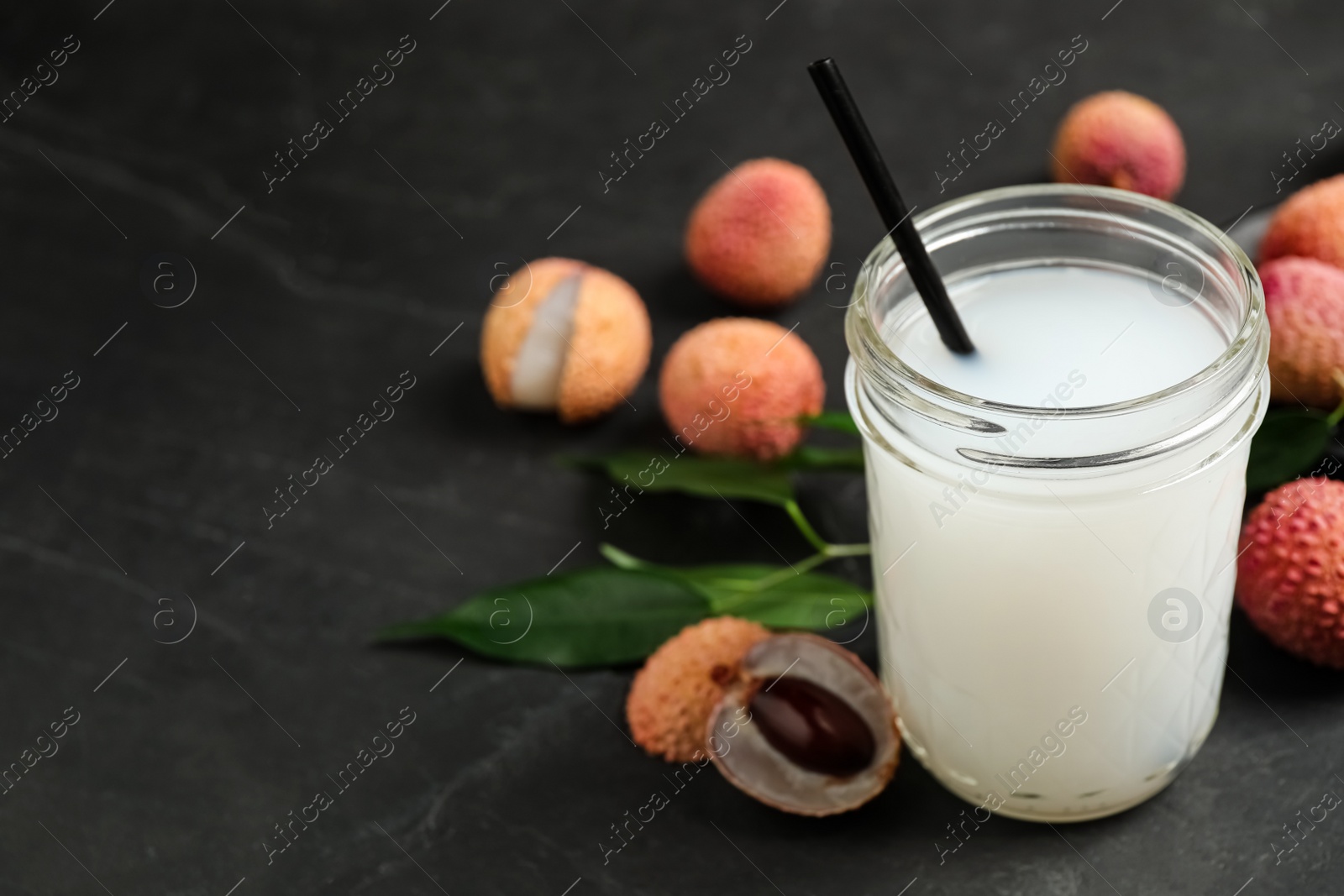 Photo of Fresh lychee juice and fruits on black table. Space for text