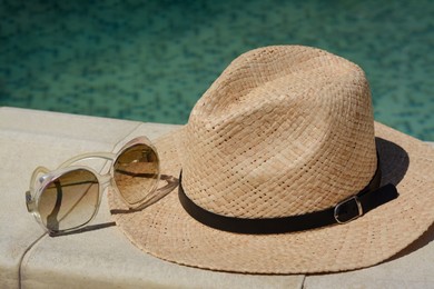 Photo of Stylish hat and sunglasses near outdoor swimming pool on sunny day, closeup. Beach accessories