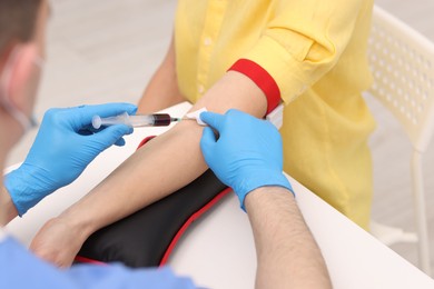 Photo of Doctor taking blood sample from patient with syringe at white table in hospital, closeup