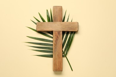 Wooden cross and palm leaf on beige background, top view. Easter attributes