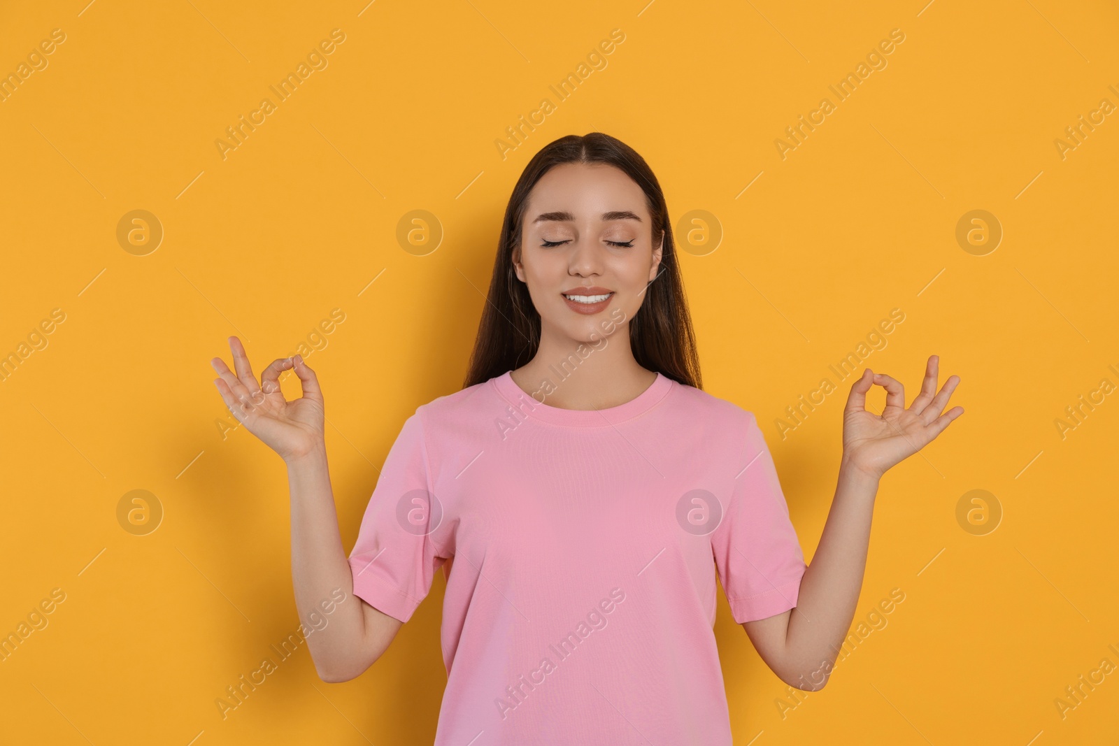 Photo of Find zen. Beautiful young woman meditating on yellow background