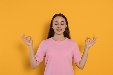 Photo of Find zen. Beautiful young woman meditating on yellow background