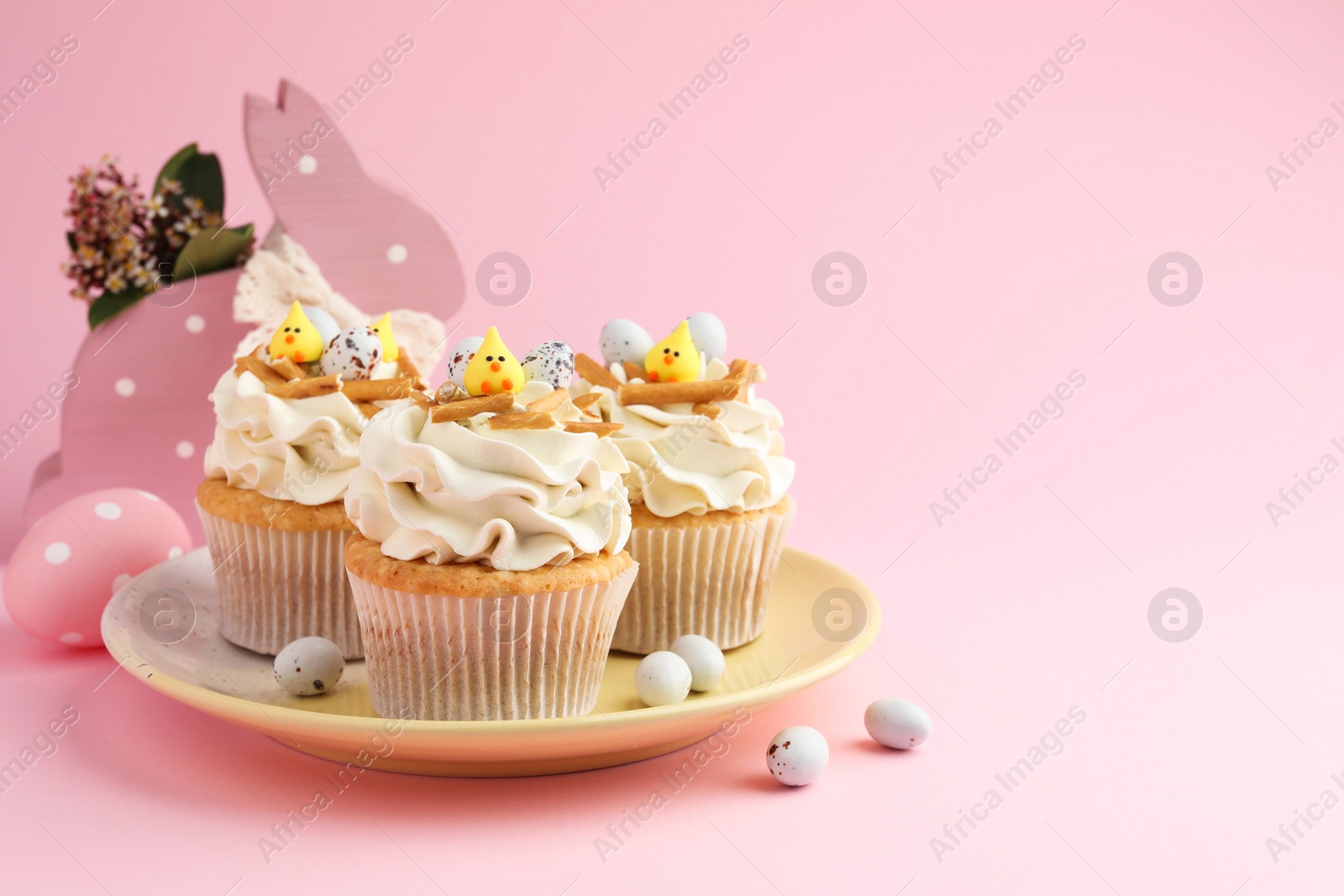 Photo of Tasty Easter cupcakes with vanilla cream and candies on pink background, space for text