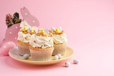 Photo of Tasty Easter cupcakes with vanilla cream and candies on pink background, space for text