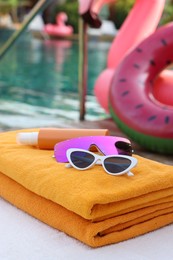 Beach towels, sunglasses and sunscreen on sunbed near outdoor swimming pool. Luxury resort