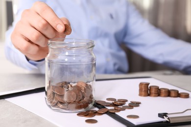 Photo of Man putting coin into glass jar at table indoors, closeup