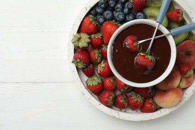 Photo of Fondue pot with chocolate and mix of fruits on white wooden table, top view. Space for text