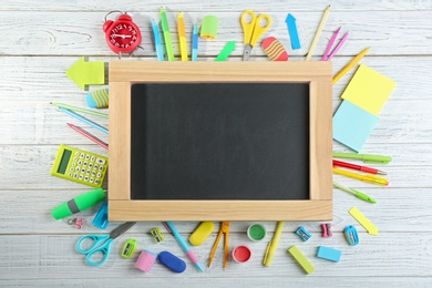 Photo of Different school stationery and blank small chalkboard on white wooden background, flat lay. Space for text