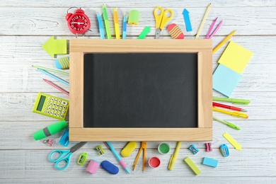 Different school stationery and blank small chalkboard on white wooden background, flat lay. Space for text